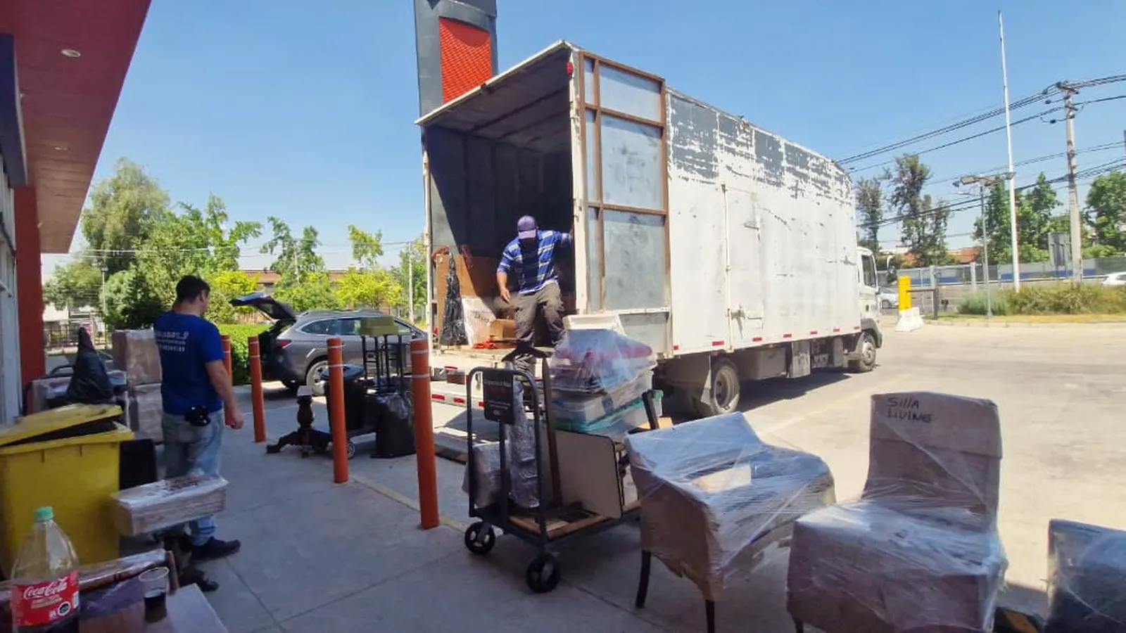 Sillas y muebles envueltos en film junto a un camión de mudanza abierto, mientras el equipo carga